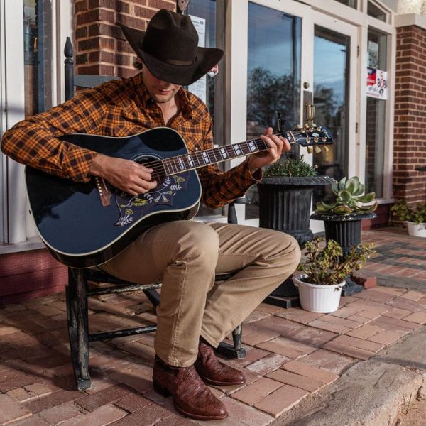 Cowboy wear a pearl snap shirt, khakis, cowboy boots and are playing guitar