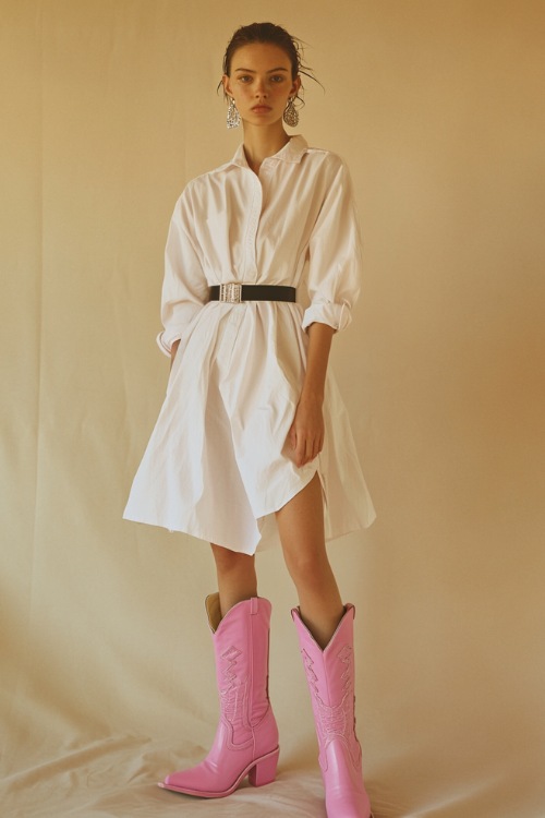 A woman in an oversized white button-down shirt worn as a dress, cinched at the waist with a wide black belt