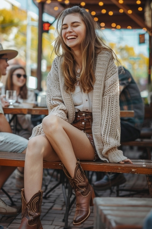 a woman wears a cardigan, a shirt, shorts and brown cowboy boots