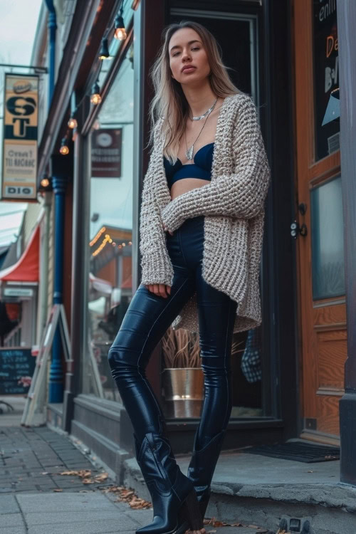 a woman wears leather leggings, black cowboy boots with a cardigan