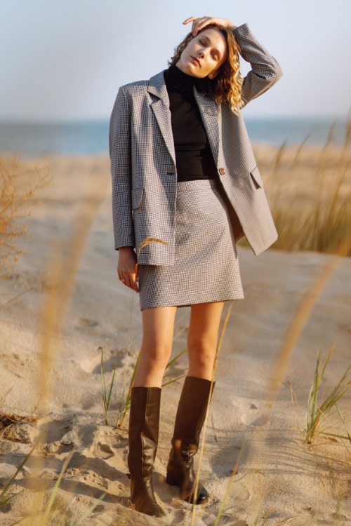 A woman wears cowboy boots with a skirt, a blazer and a black turtle neck