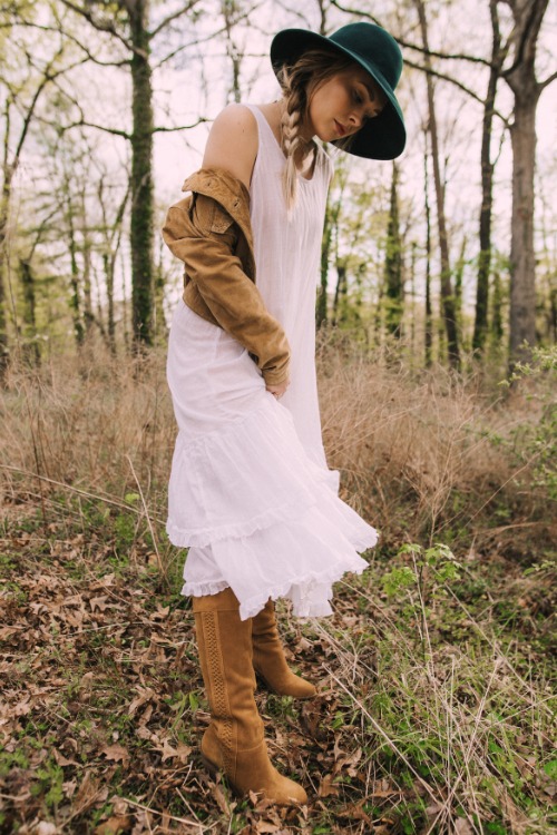 a woman wears cowboy boots with a tiered lace dress and a coat