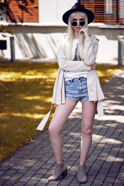 A woman wears cowboy boots with denim shorts, simple white tee and a coat