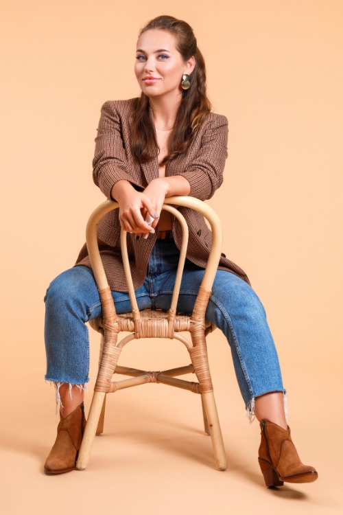 a woman wears cowboy boots with ripped hem jeans, striped blazer and a pink top