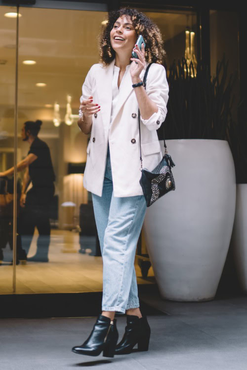 A woman wears jeans, black ankle cowboy boots, blazer and a white tee