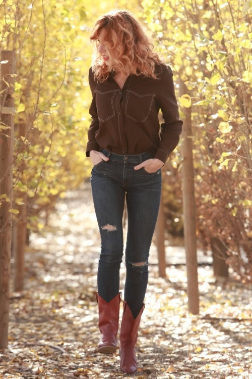 a woman wears brown cowboy boots with ripped jeans in the forest