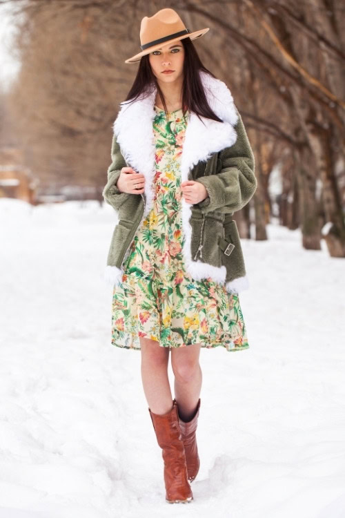 a woman wears cowboy boots with a pattern dress and warm green coat for winter