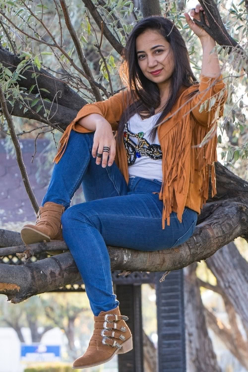a woman wears cowboy boots with jeans and a fringe jacket