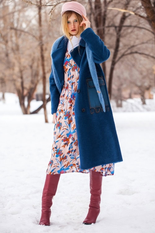 a woman wears red cowboy boots with a pattern dress and warm blue coat for winter