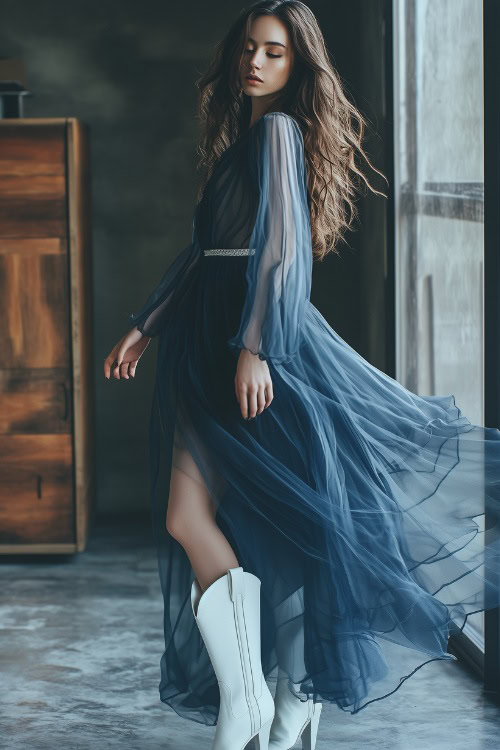 A fashion-forward woman in a sheer chiffon navy blue dress with white cowboy boots, elegantly standing in a modern studio