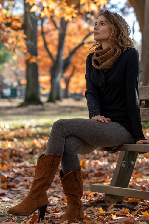 A woman wears brown cowboy boots with leggings, sweater and a scarf