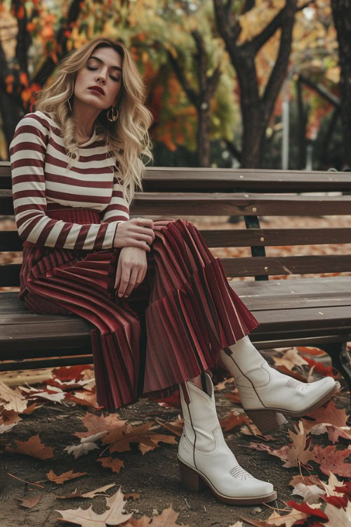 A woman wears white ankle cowboy boots with a pleated red skirt and a striped top