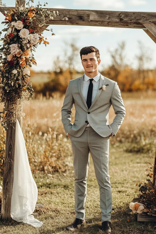 A groomsman wears a light gray suit with black cowboy boots and a black tie