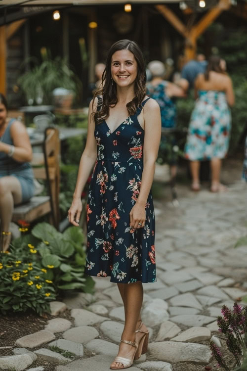 A woman wears a navy blue floral wedding guest dress with beige block heels