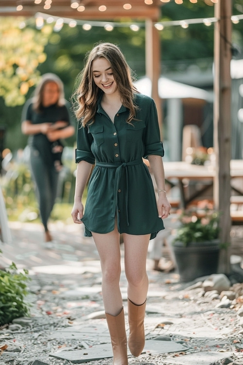 A woman wears a short dark green shirt-style wedding guest dress with tan boots