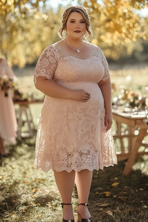 A plus-size woman wears a blush pink lace wedding guest dress with black heels