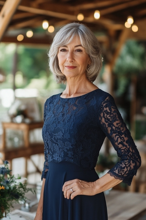 A woman over 50 wears a navy blue long-sleeve wedding guest dress with lace details on the bodice and sleeves