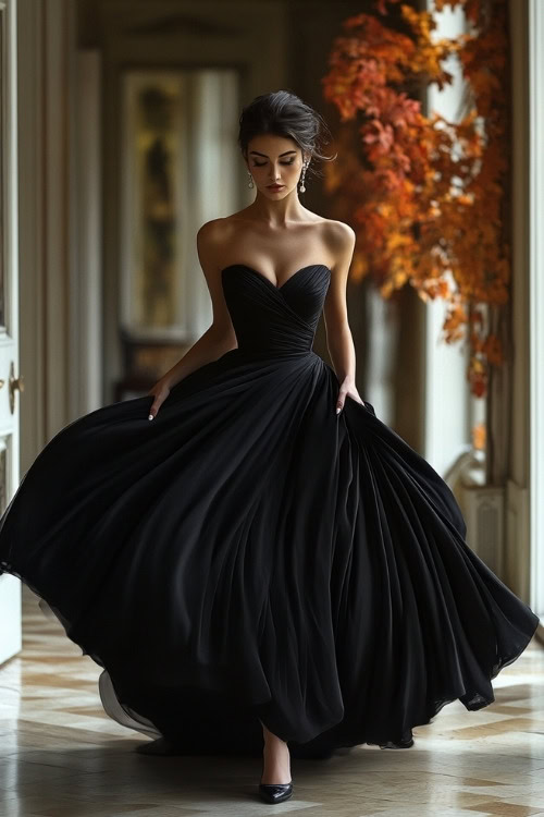 A woman wears a black strapless wedding guest dress with a flowing pleated skirt and black heels