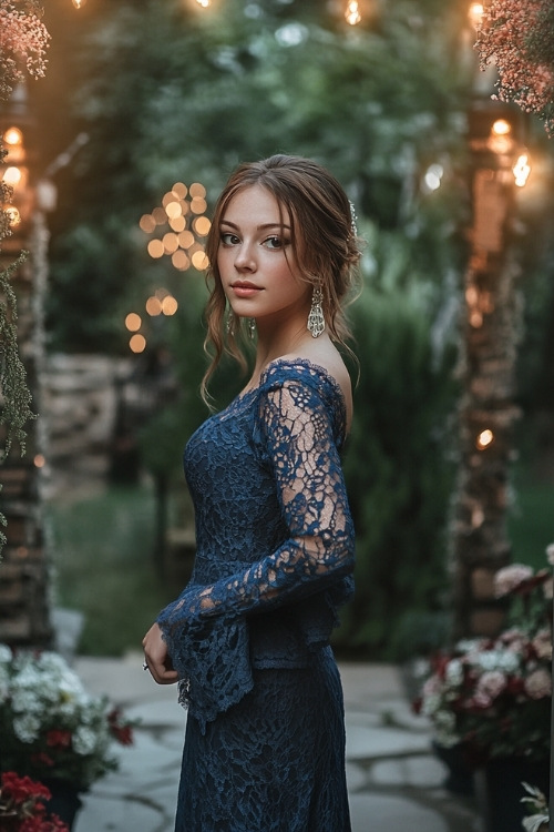 A woman wears a navy blue lace wedding guest dress with long sleeves and bell cuffs