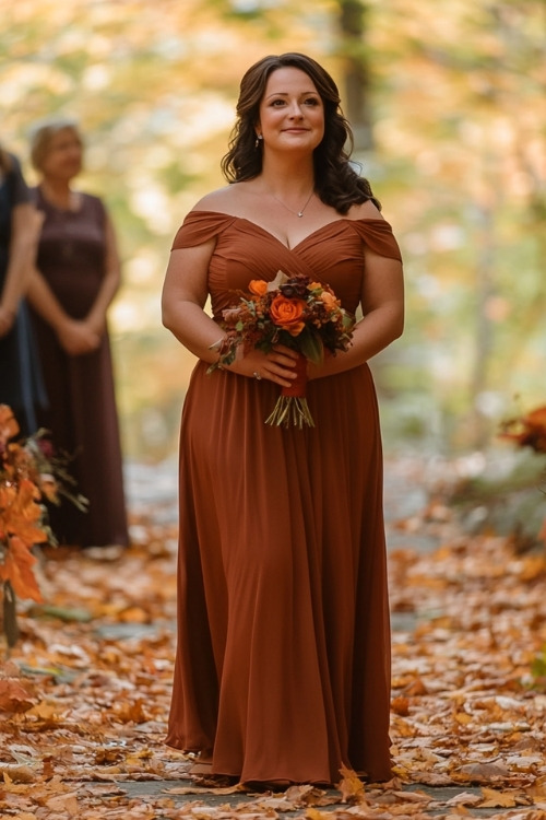 a plus size woman wears a rust wedding guest dress with an off shoulder design