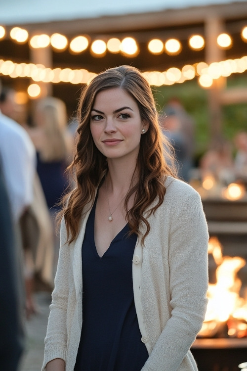 A woman wears a navy dress with a cream jacket, standing at a vineyard wedding reception with outdoor fire pits (2)