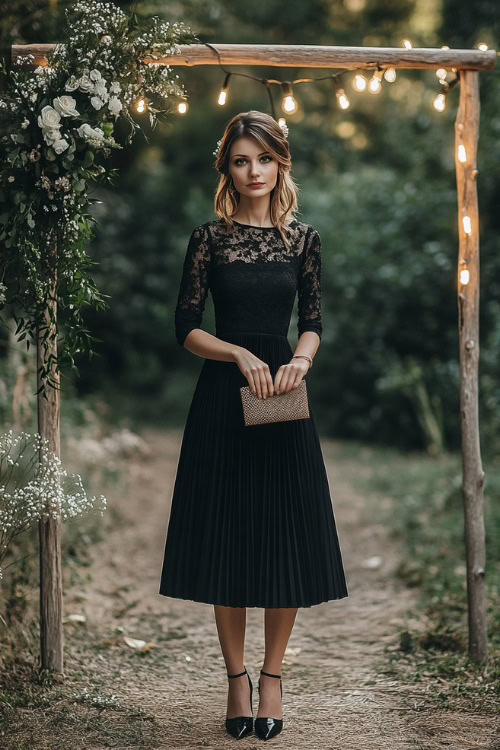 A woman wearing a black tea-length dress with lace sleeves and a soft pleated skirt, accessorized with heels and a clutch (2)