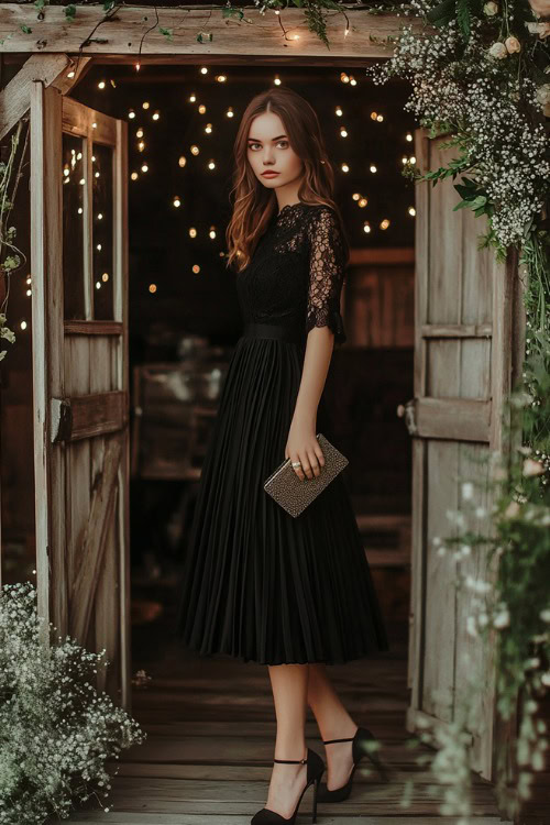 A woman wearing a black tea-length dress with lace sleeves and a soft pleated skirt, with heels and a clutch