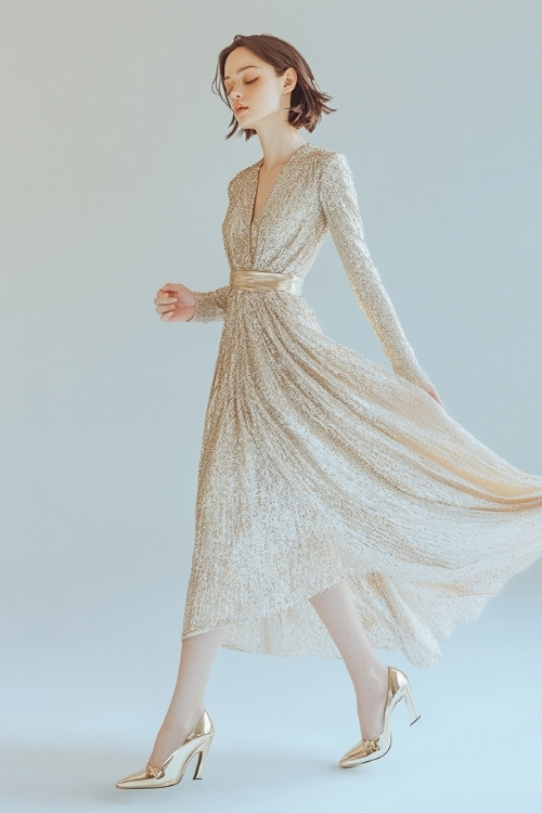 A woman wearing a shimmering champagne midi dress with a wrap-style bodice, long sleeves, and a flared hem,