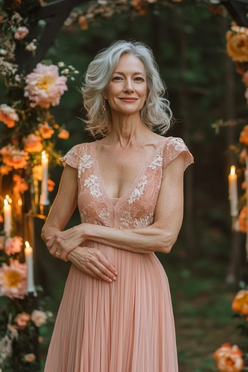 A chic woman over 50 in a pastel peach sleeveless maxi dress with a cinched waist, a tiered hemline, and subtle lace detailing