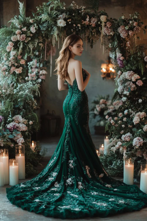 A woman in a deep emerald green mermaid gown with a sweetheart neckline, floral lace appliqués, and a long flowing train