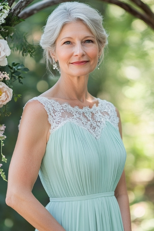 A woman over 50 in a pastel mint green sleeveless midi dress with a pleated hemline, a square neckline, and lace accents