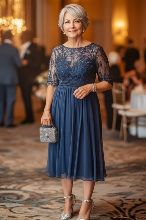 A petite woman over 50 in a tea-length dark blue chiffon dress with a high neckline and sheer sleeves