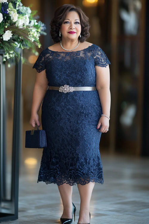 A plus-size woman over 40 in a sophisticated navy blue midi dress with lace overlay and cap sleeves, paired with a satin belt 