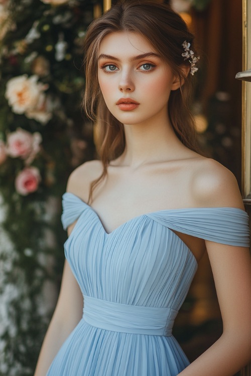 A woman in a baby blue midi-length pleated dress with a cinched waist, standing near an elegant wedding ceremony entrance with floral-adorned pillars