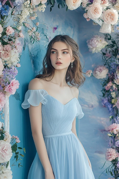 A woman in a sky-blue knee-length cocktail dress with cap sleeves and a fitted bodice, standing beside a floral wedding arch with soft pastel decorations