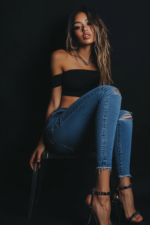 A woman styled in a one-shoulder bodysuit tucked into distressed mom jeans, paired with ankle-strap heels and a chain necklace